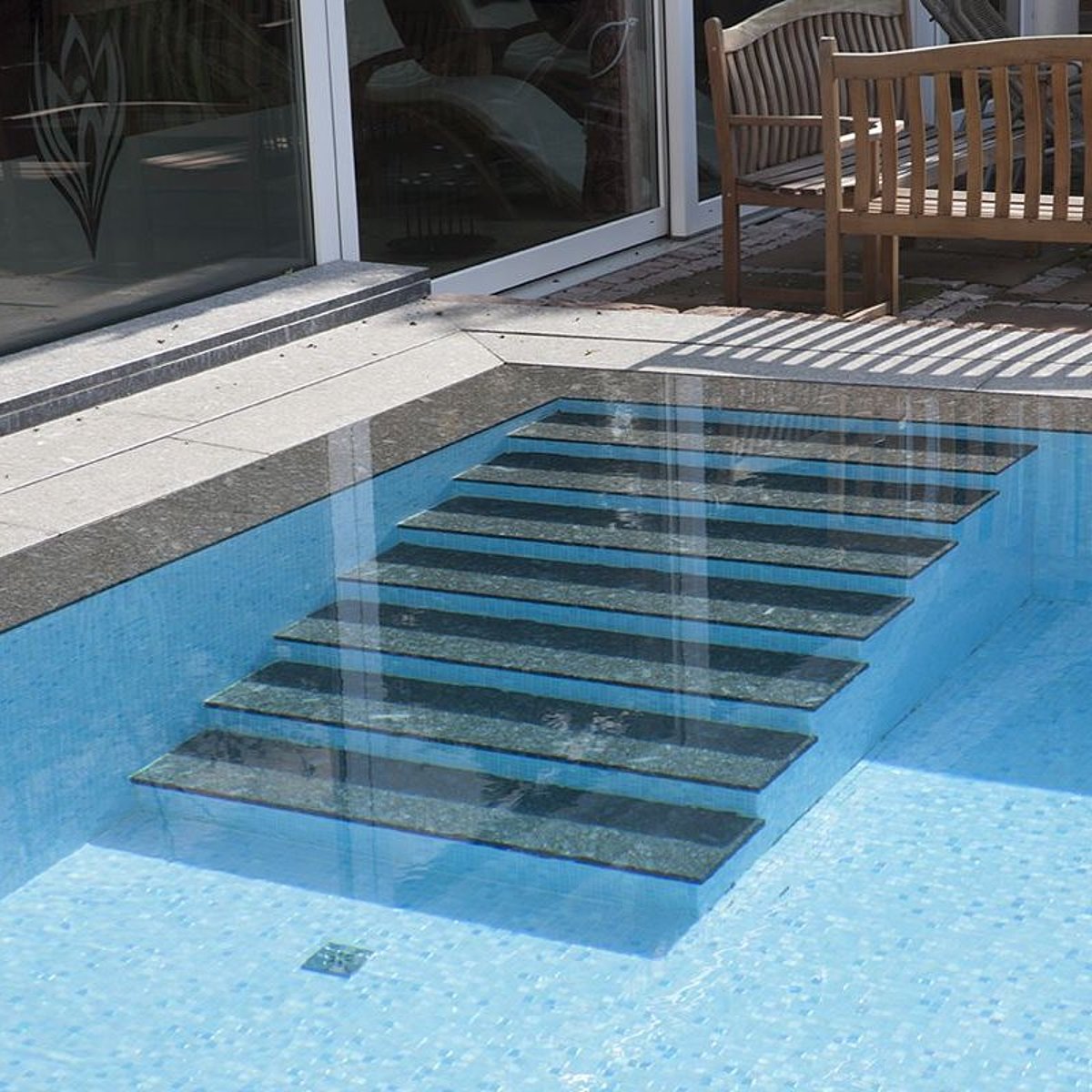 Ein Swimming Pool mit Einstiegstreppe, die mit Naturstein gestaltet wurde – passend zum Beckenumlauf.