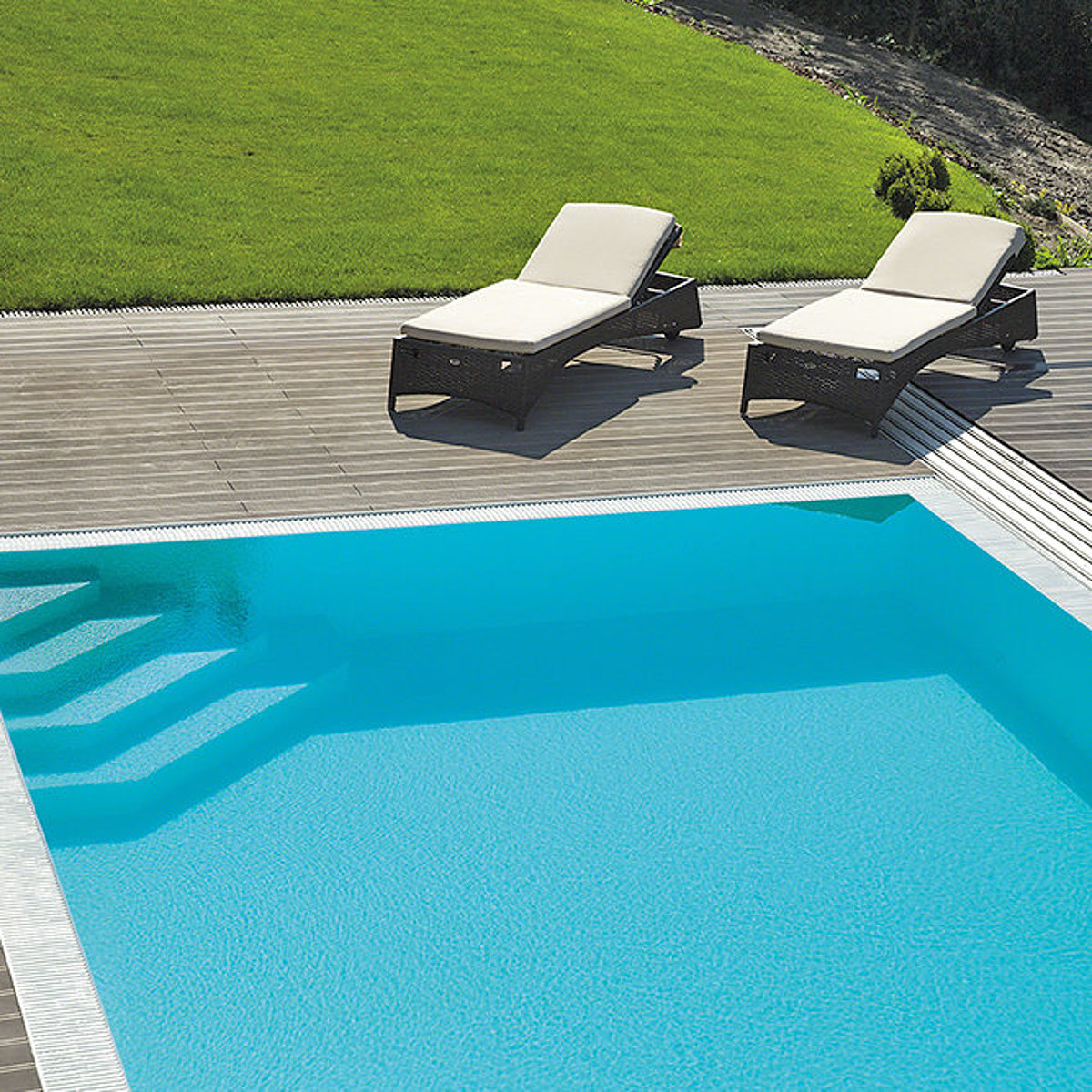 Een polystone-zwembad met trap om de hoek in de tuin. Aan de rand van het zwembad: twee ligstoelen.
