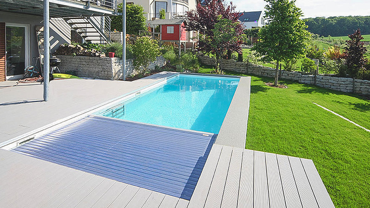 In eine Terrasse eingelassenes Skimmerbecken mit halbgeschlossener Rollladenabdeckung. 