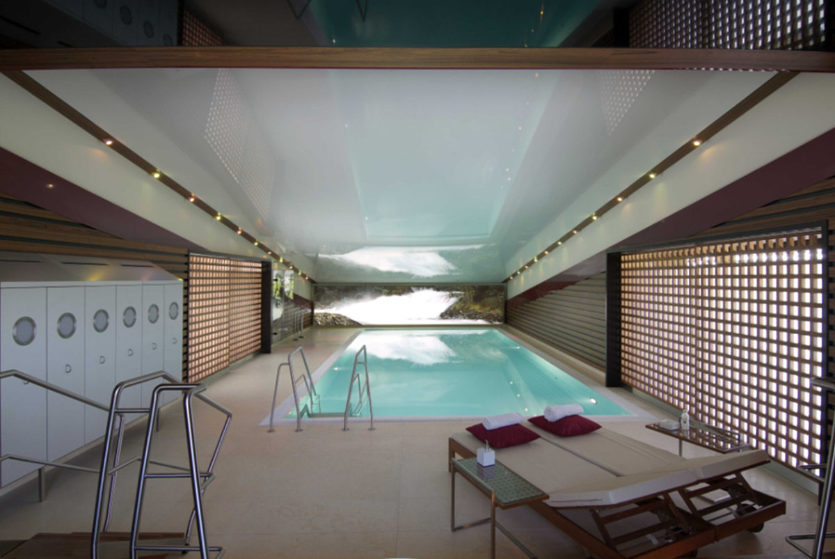 Ein Indoor-Pool mit einer Liege im Vordergrund.