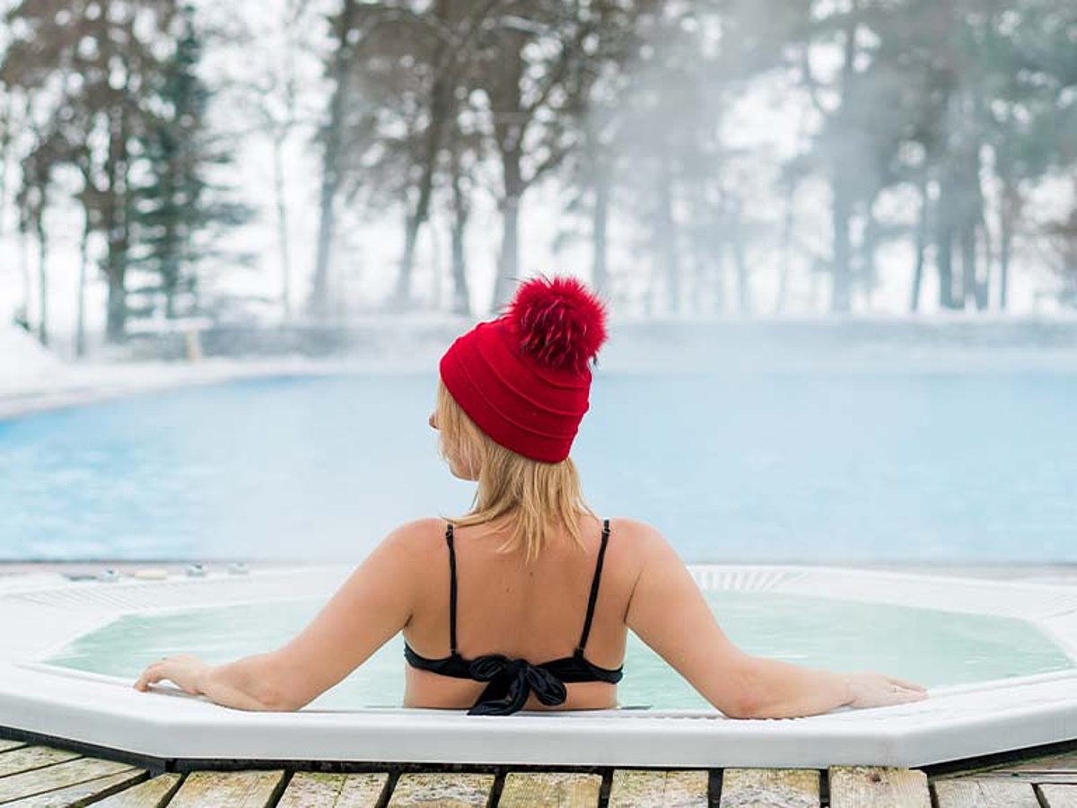 Eine Frau sitzt mit Wollmütze und Bikini bekleidet im winterfesten Whirlpool.