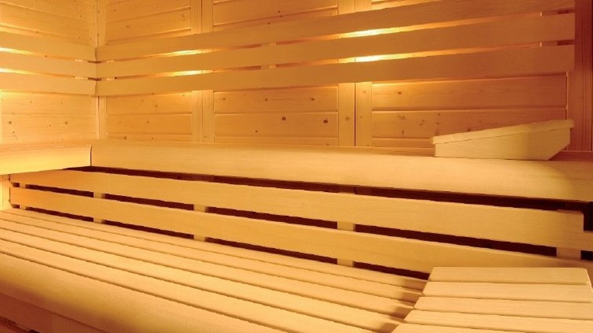 Interieur van een sauna met verlichte rugleuningen achter de bovenste bank.