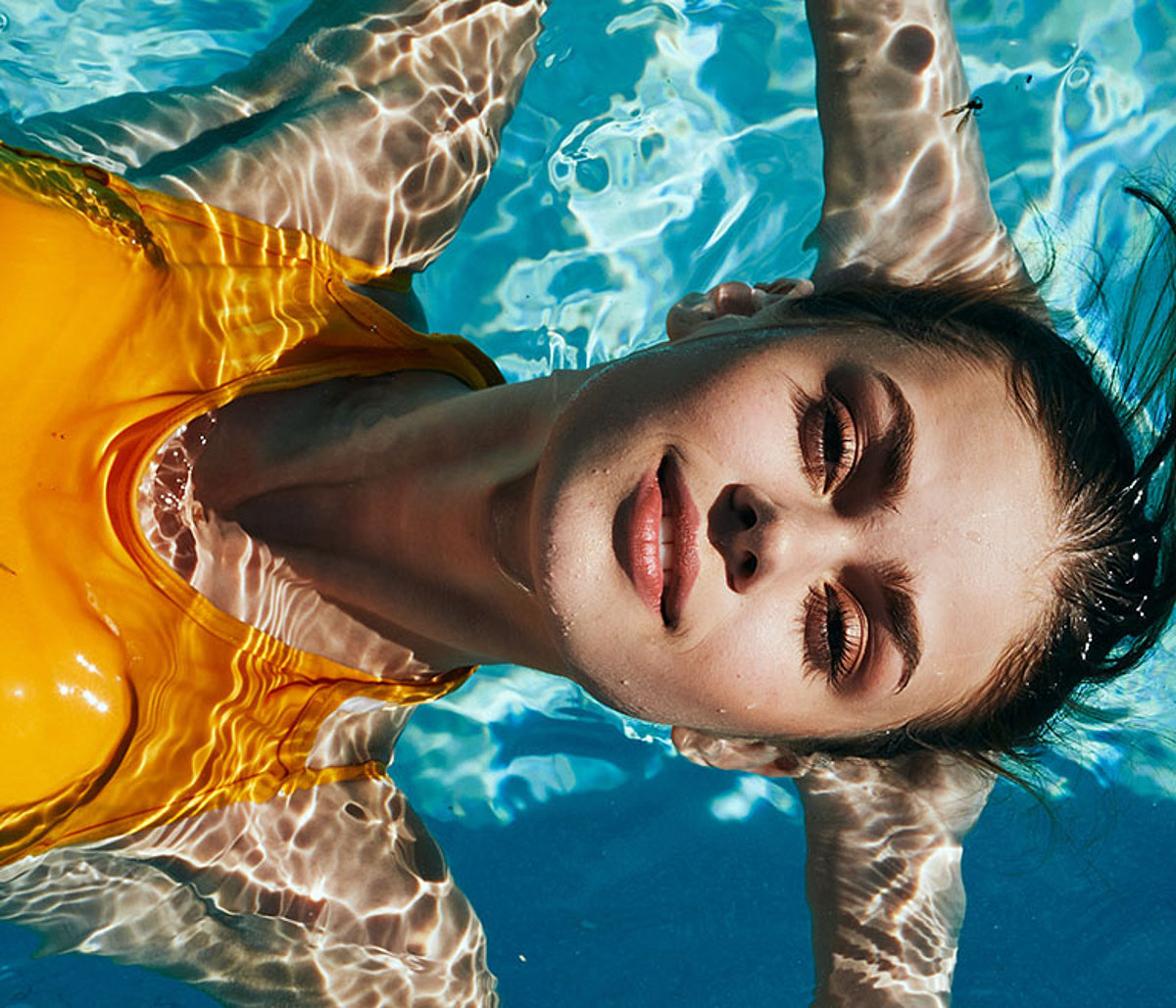 Eine Frau treibt mit geschlossenen Augen auf dem Rücken entspannt in einem Pool.