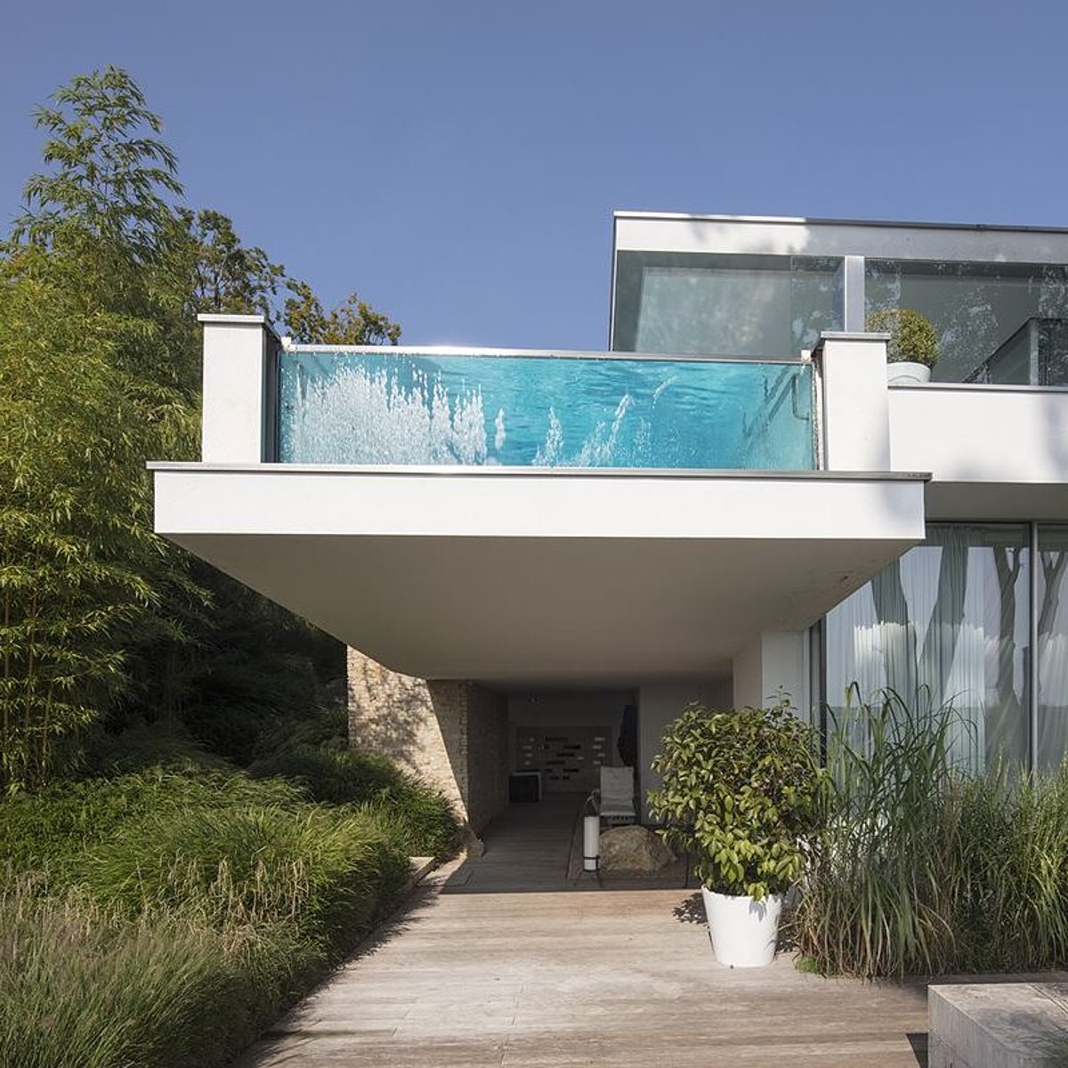Een zwevend betonnen bassin aan de zijkant van een huis met een inzetstuk van glas aan de voorkant.