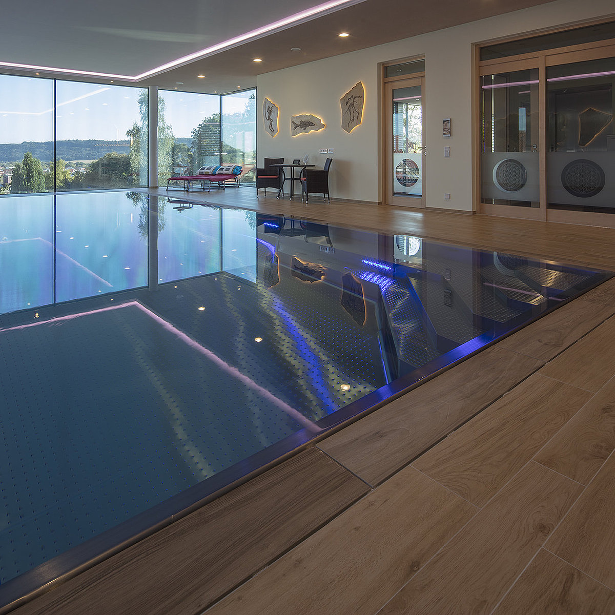 Binnenzwembad met blauwe verlichting en grote ramen aan de voorkant.