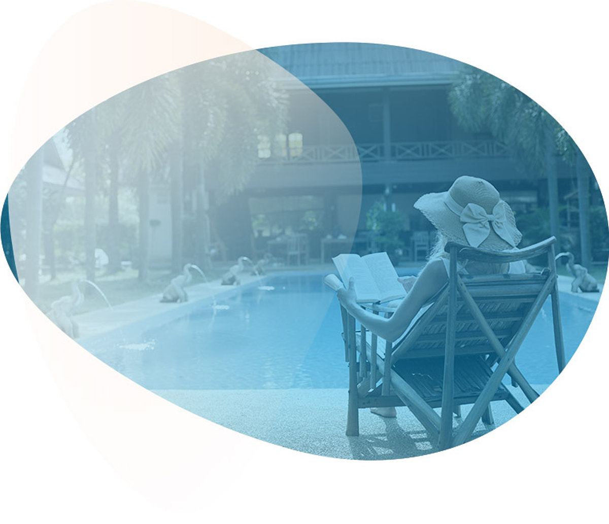 Eine Frau mit Sonnenhut sitzt am Pool und liest ein Buch.