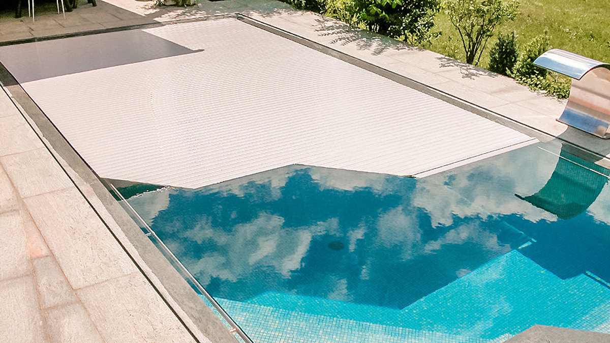 Ein Pool mit besonderer Beckenform und speziell dafür angefertigter Rollladenabdeckung.
