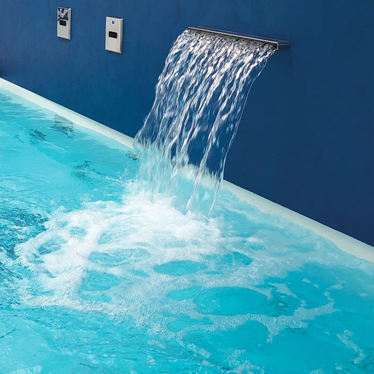 De Aquello waterval geïntegreerd in een muur naast de rand van het zwembad. Het water stroomt in het zwembad.