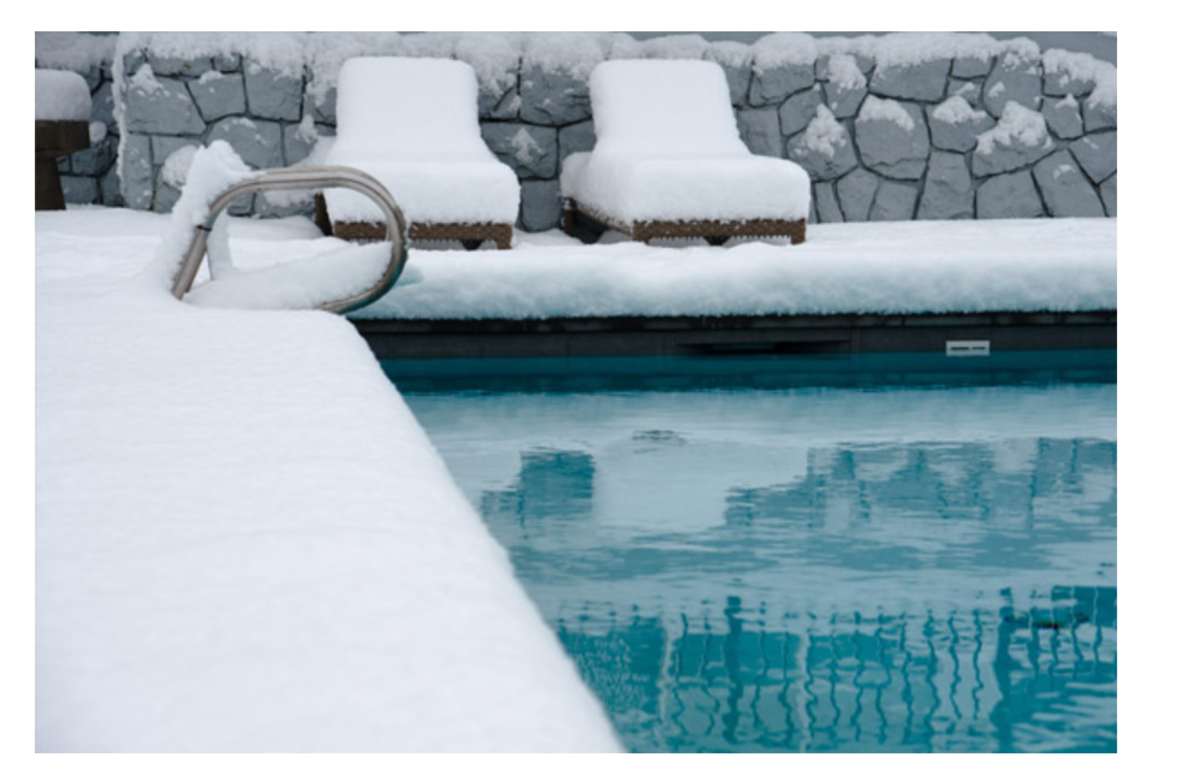 Ein Pool. Die Poolumgebung inklusive Poolliegen sind schneebeckt.