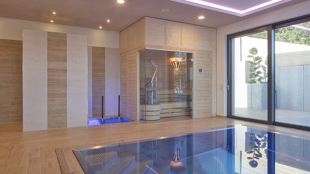 Een moderne massief houten sauna in een zwemhal naast een dompelbad. Ervoor: een zwembad.