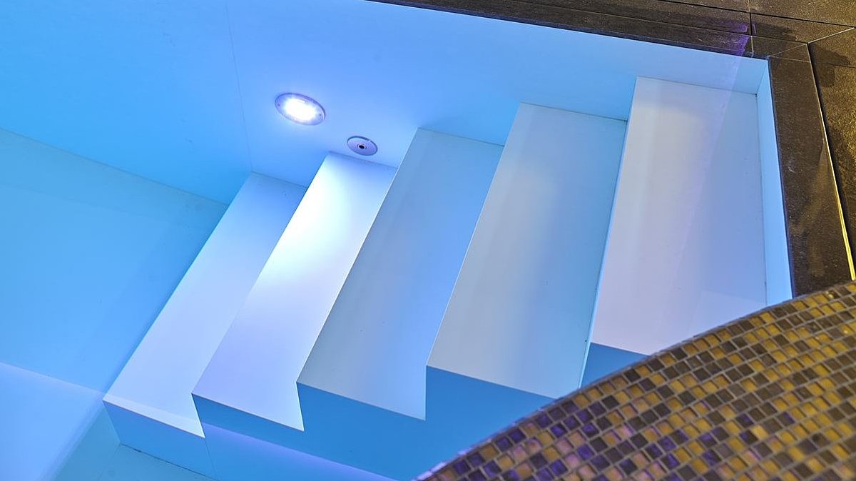 Ein Pool mit Treppe und LED-Strahler auf Höhe der untersten Stufe.