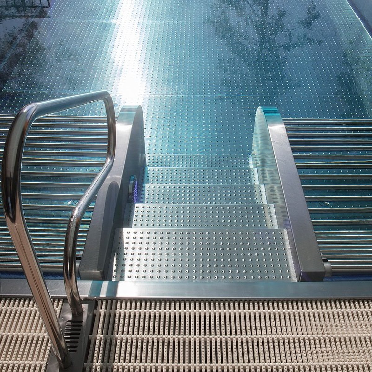 Ein Outdoor-Pool aus Edelstahl mit Einstiegstreppe, die über einen Handlauf verfügt. Links und rechts neben der Treppe befindet sich jeweils eine Sprudelliege.
