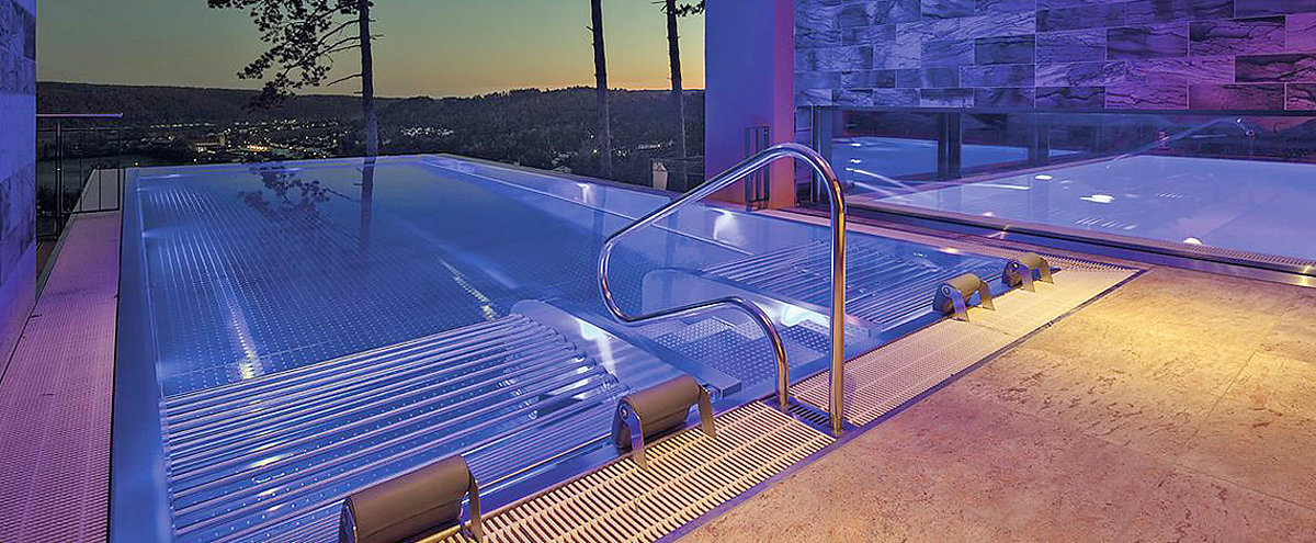 Ein beleuchteter Infinity-Pool mit Einstiegstreppe und Sprudelliegen.
