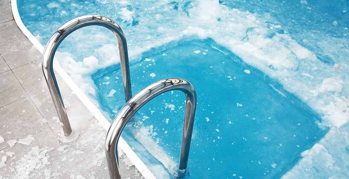 Een zwembad - het zwemoppervlak is bevroren. Een rechthoekig gebied in de buurt van de zwembadtrap is vrijgemaakt van ijs. 