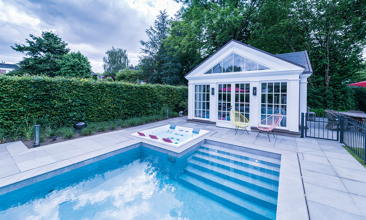 Außenschwimmbecken mit integriertem Whirlpool und breiter Einstiegstreppe daneben. In direkter Poolnähe: ein Poolhaus.