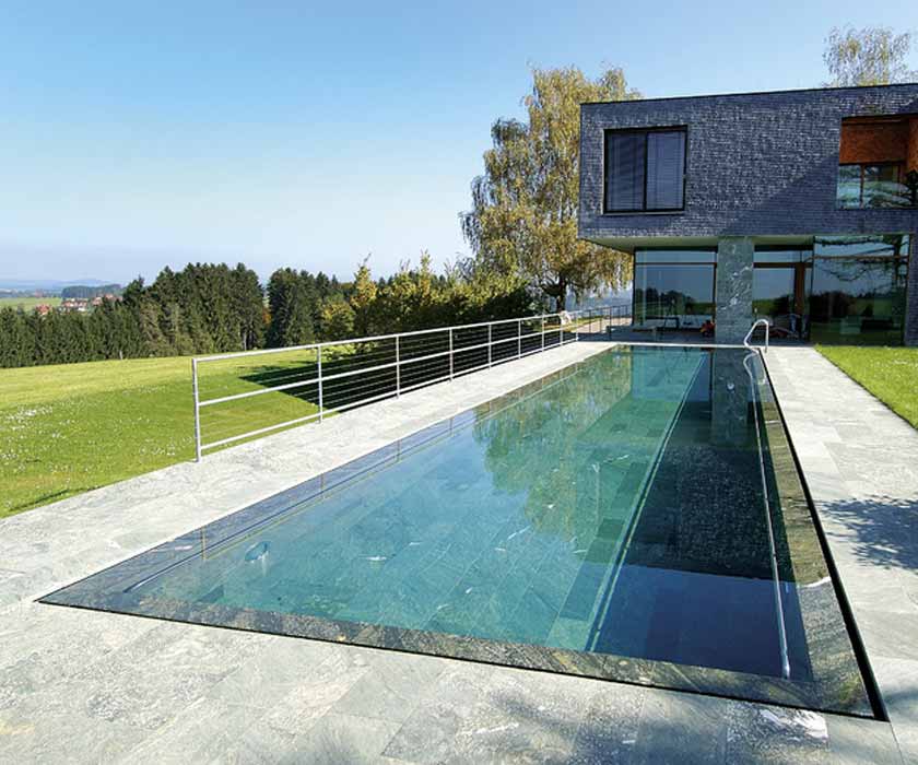 Een zwembad met granieten overloopgoot. Op de achtergrond: een woonhuis.