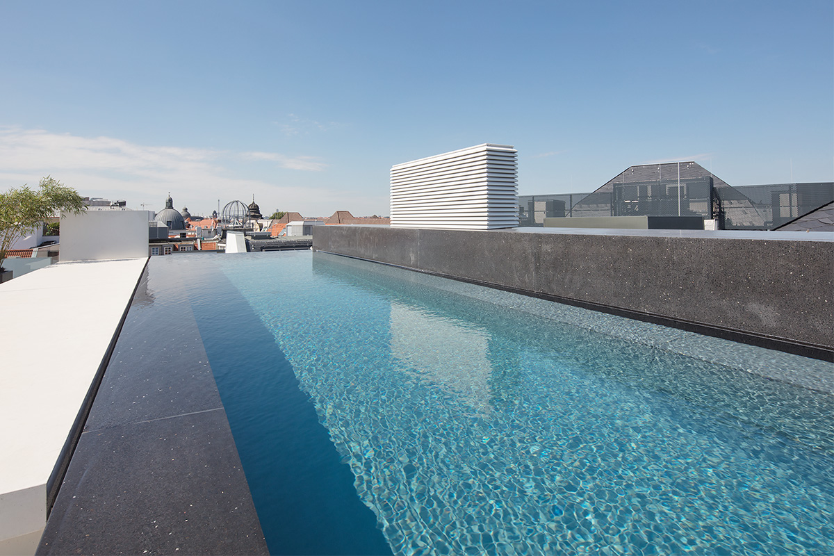 Infinity-Pool aus Beton mit blauem Wasser, von dem aus man auf eine Stadt raufschauen kann.