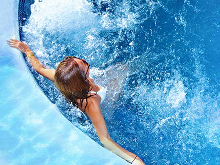 Een vrouw met een zonnebril staat in het zwembad voor de massagestralen.